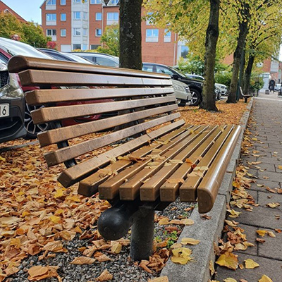 Eine hölzerne Parkbank mit Herbstblättern rundherum auf dem Boden.